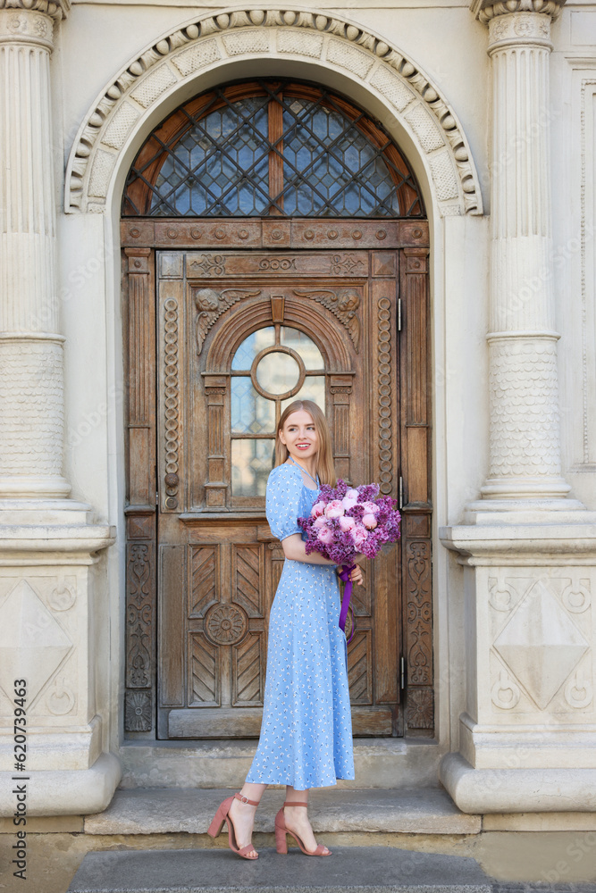 Beautiful woman with bouquet of spring flowers near building outdoors Beautiful woman with bouquet of spring flowers near building outdoors