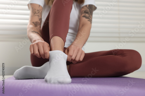 Woman putting on white socks on exercise mat indoors, closeup