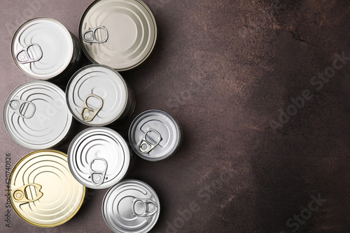 Many closed tin cans on brown table, flat lay. Space for text