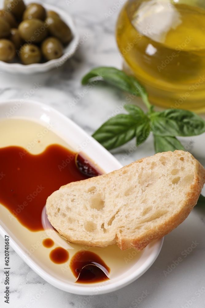 Bowl of organic balsamic vinegar with oil served with bread slice, basil and olives on white marble table Bowl of organic balsamic vinegar with oil served with bread slice, basil and olives on white marble table