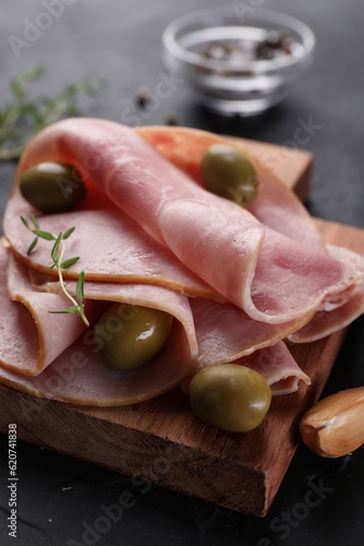 Tasty ham with olives, garlic and thyme on black table, closeup