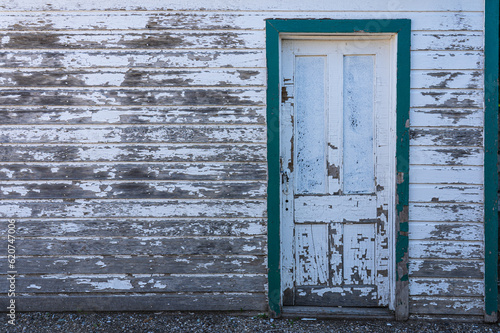 Old closed door on building is framed with green. Aged structure is weathered wood with white paint peeling. 