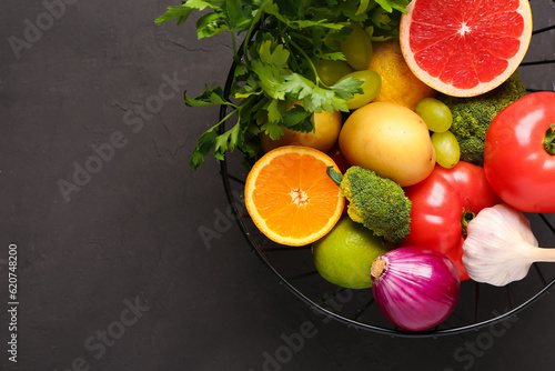 Basket with different fresh fruits and vegetables on black background, closeup
