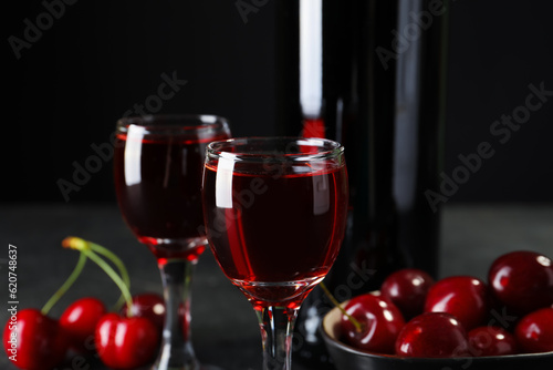 Glasses and bottle with sweet cherry liqueur on black background