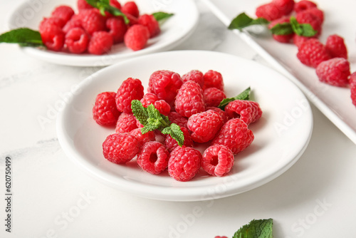 Plates with fresh raspberries and mint on white background