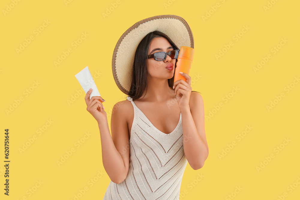 Beautiful young woman with sunscreen cream blowing kiss on yellow background Beautiful young woman with sunscreen cream blowing kiss on yellow background