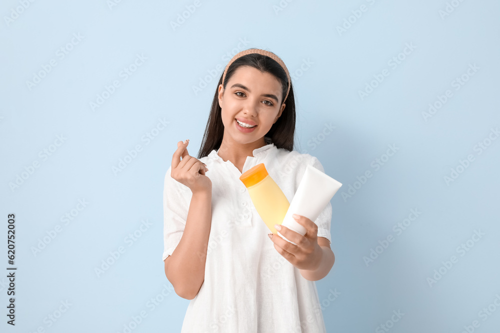 Beautiful young woman with bottles of sunscreen cream making heart gesture on light background Beautiful young woman with bottles of sunscreen cream making heart gesture on light background