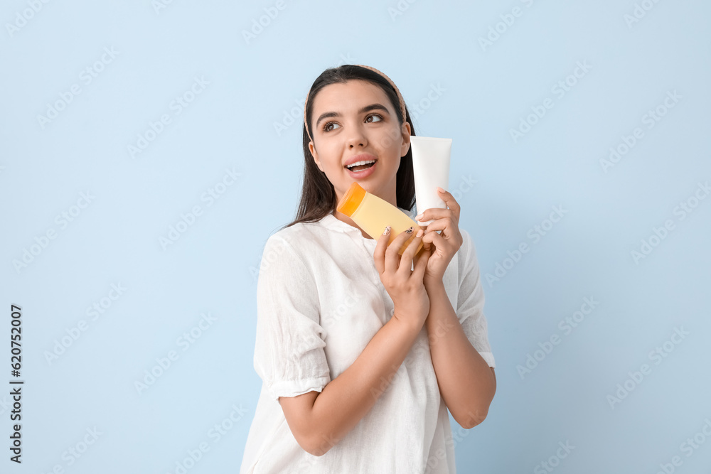 Beautiful young woman with bottles of sunscreen cream on light background Beautiful young woman with bottles of sunscreen cream on light background