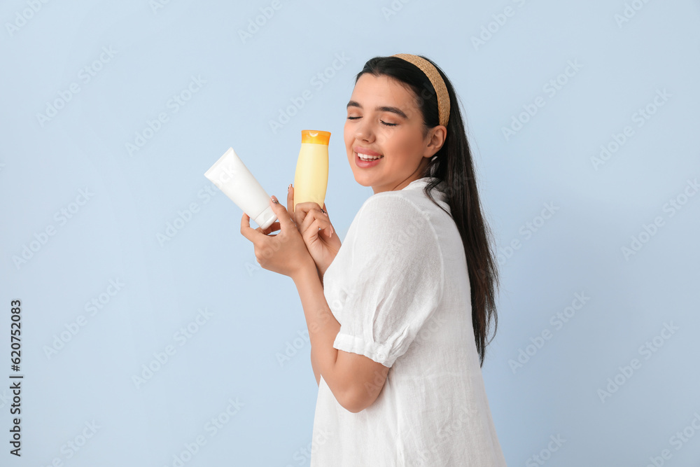 Beautiful young woman with bottles of sunscreen cream on light background Beautiful young woman with bottles of sunscreen cream on light background
