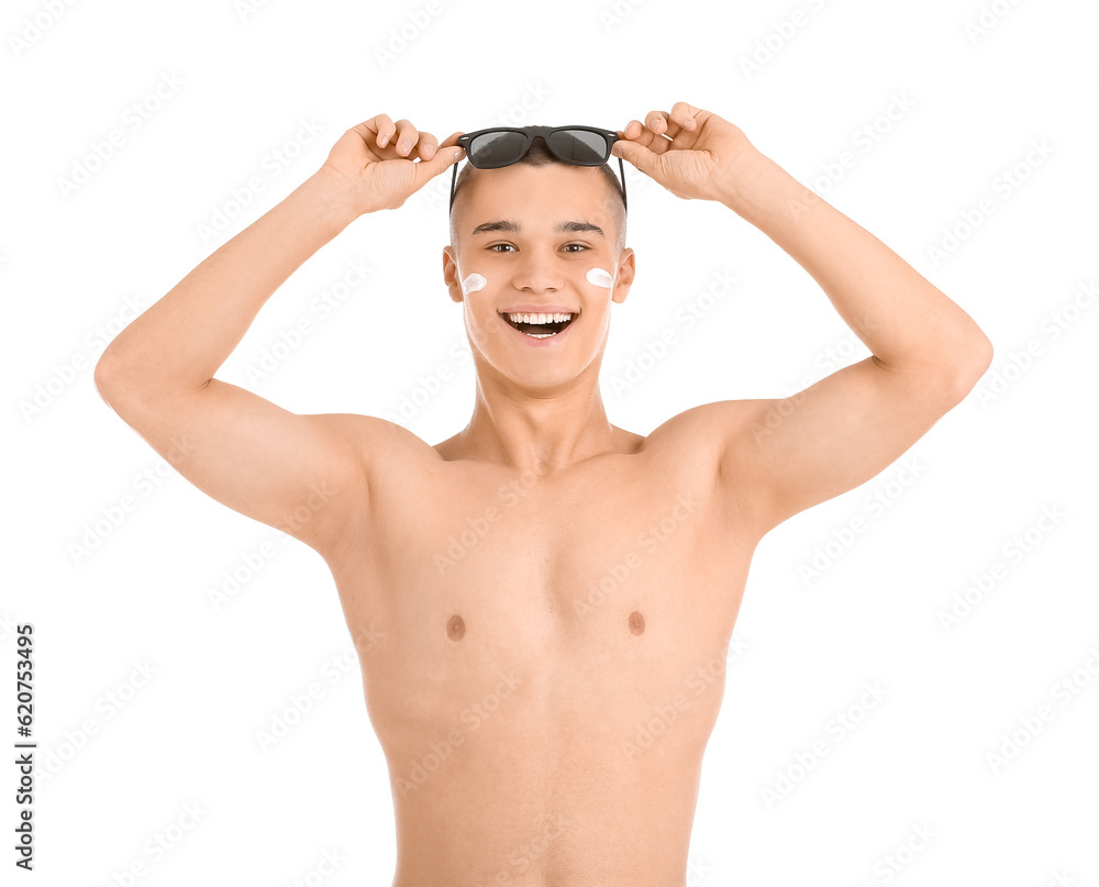 Happy young man with sunglasses and sunscreen cream on his face against white background