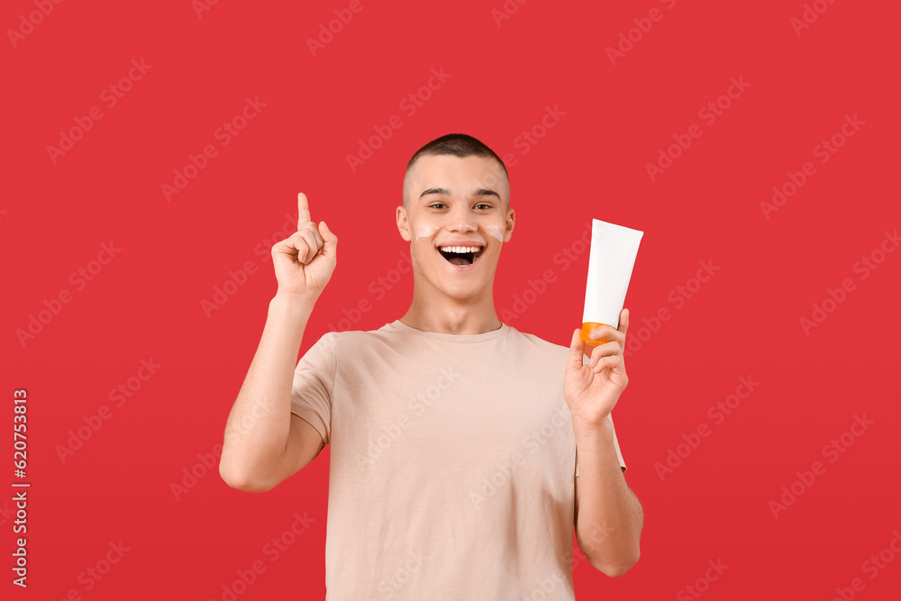 Happy young man with bottle of sunscreen cream on red background Happy young man with bottle of sunscreen cream on red background