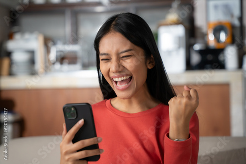 Obraz na plátne Beautiful asian young woman looking mobile phone laughing with good news at living room
