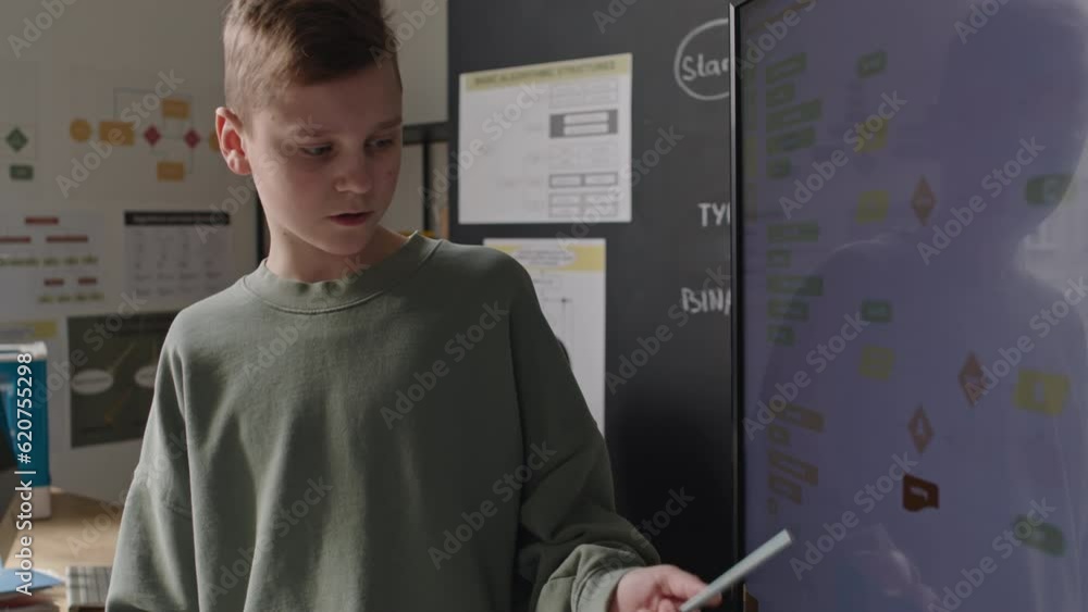 Boy explaining computer algorithm scheme on digital screen while giving presentation during programming lesson at school, black teacher listening in background Boy explaining computer algorithm scheme on digital screen while giving presentation during programming lesson at school, black teacher listening in background