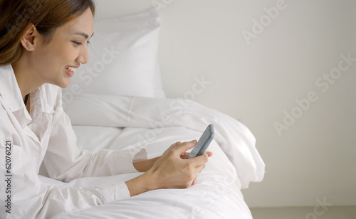 Relaxed woman using smart phone in the morning in bed at home.