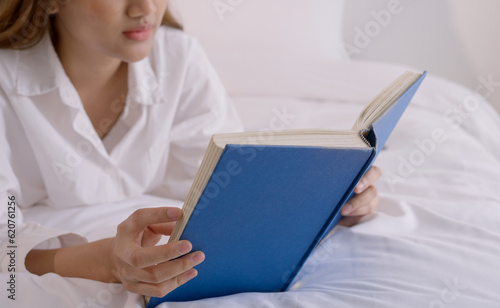 Young woman reading book on bed at home.