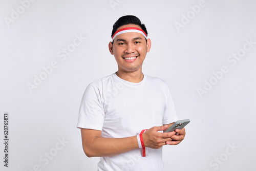 Smiling young Asian men celebrate Indonesian independence day on 17 August while holding mobile phone isolated over white background