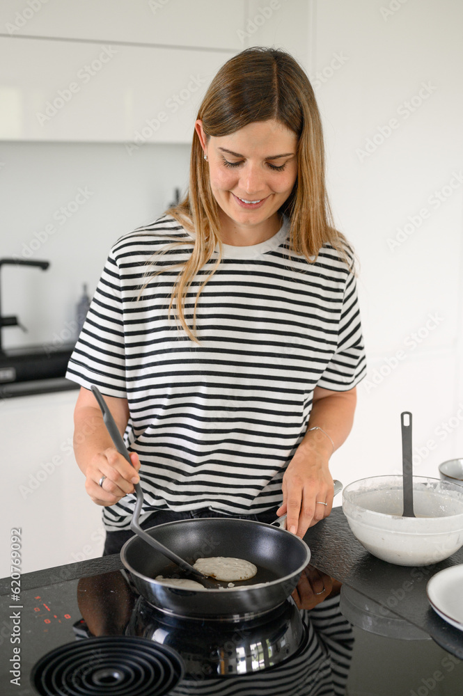 Smiling young woman frying pan in kitchen Smiling young woman frying pan in kitchen
