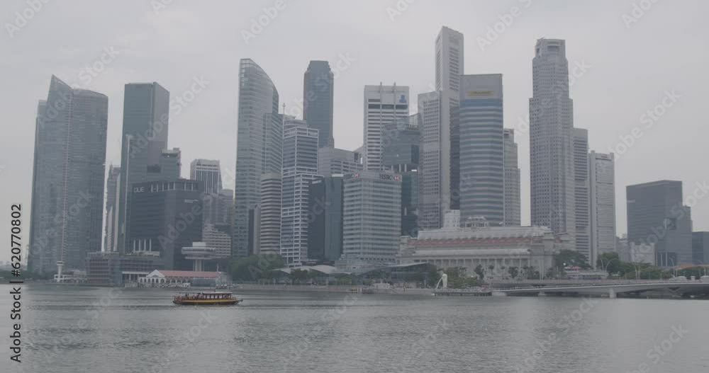 Wide shot: Static camera captures the impressive architecture of the Singapore skyline on a gray day, with water and ships in the foreground. Everything in focus Wide shot: Static camera captures the impressive architecture of the Singapore skyline on a gray day, with water and ships in the foreground. Everything in focus
