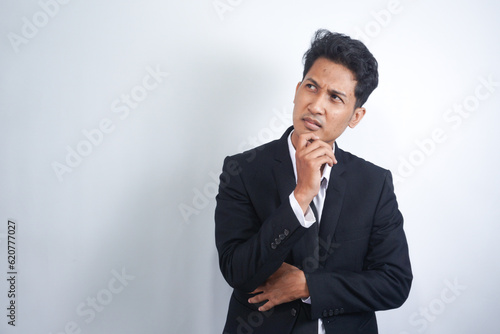 Thoughtful male customer thinking hard, looking away at copy space, leaning chin on hand. Handsome young man in suit standing isolated over white background. Special offer concept