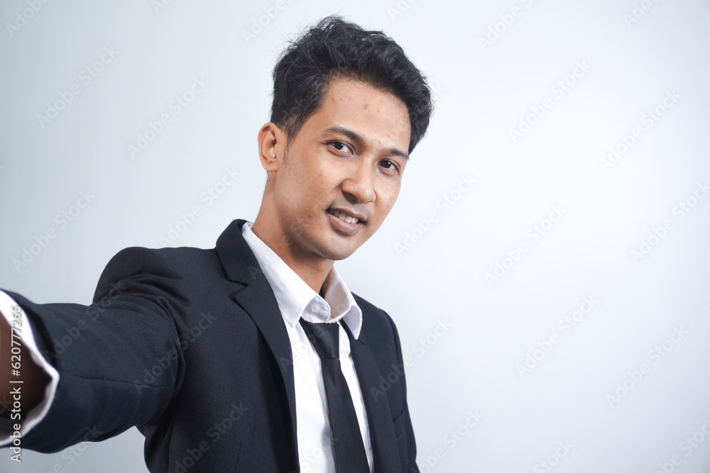 Handsome young man wearing suit taking a selfie by his phone, standing on a white background. Handsome young man wearing suit taking a selfie by his phone, standing on a white background.