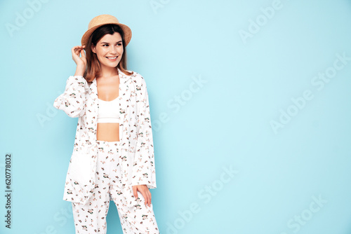 Young beautiful smiling female in trendy summer costume clothes. Carefree woman posing near blue wall in studio. Positive model having fun indoors. Cheerful and happy. In hat