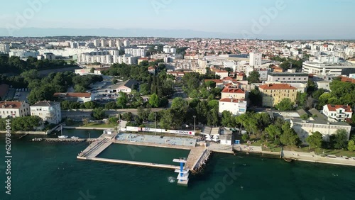 Flying backwards with drone, summer afternoon Zadar, Croatia. Coastal pool with diving platform and city photo