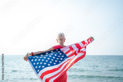 Mature woman holding US flag enjoying time at the beach. #620794476