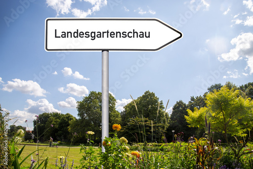 Symbolbild Landesgartenschau: Richtungspfeil mit der Aufschrift Landesgartenschau in einem Park (Compsosing)