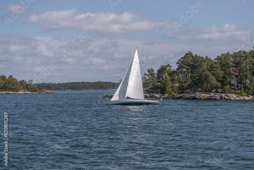 Island, skerries and islet, in the middle part of the archipelago. A old style wood sail boat passing a small island, a sunny summer day in Stockholm