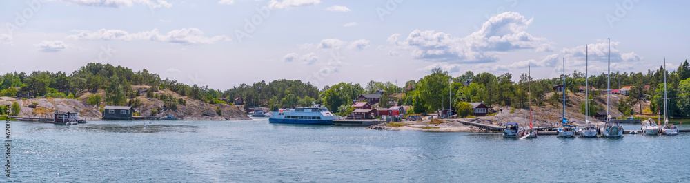 Fototapeta premium Island, skerries, islet, in the archipelago, houses, boat sheeds, jetties. Old steam passenger and sail boat passing the island Möja on the bay , a sunny summer day in Stockholm