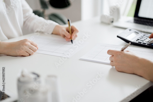 Two accountants using a calculator and laptop computer for counting taxes or revenue balance while rolls of receipts are waiting to be calculating. Business audit and taxes concepts