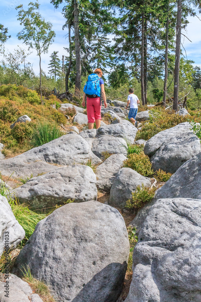 Two tourists walsking on the red hiking trail between the rock towns of Błędne Skały and Szczeliniec Wielki in the Central Sudetes in the Stolowe Mountains (Poland) Two tourists walsking on the red hiking trail between the rock towns of Błędne Skały and Szczeliniec Wielki in the Central Sudetes in the Stolowe Mountains (Poland)