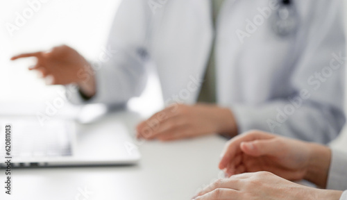 Doctor and patient sitting at the desk in clinic office. The focus is on female physician s hands pointing to laptop computer monitor  close up. Perfect medical service and medicine concept