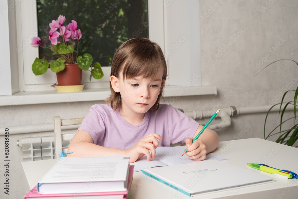 Girl sits at a table with books and a notebook and writes with her left hand. Left handed child. Girl sits at a table with books and a notebook and writes with her left hand. Left handed child.