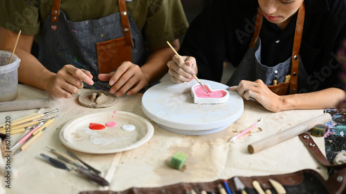 Cropped shot of man decorating clay plate on table at ceramic workshop. Indoors lifestyle activity and hobbies concept