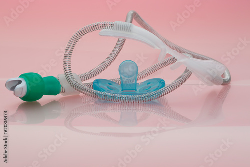 Concept of sick baby. Light blue dummy and nasal oxygen cannula for neonates in intensive care units in need of increased airflow with high-flow oxygen therapy placed on rose background