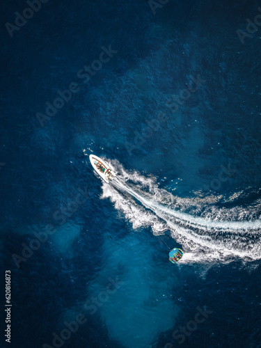 Aerial view of a motor speeboat towing a watersports fun inflatable tube over blue sea