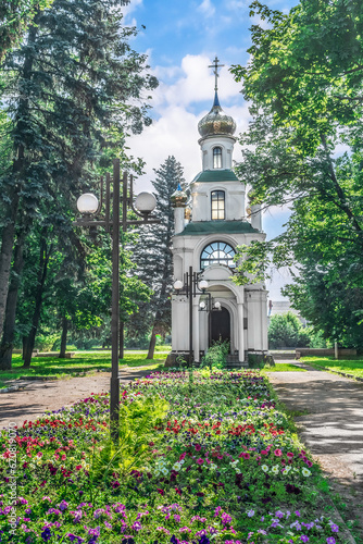 Trostyanets, Sumy Oblast, Ukraine - June 18, 2023: Kaplytsya Vsikh Svyatykh in the city park in Trostyanets. A small Orthodox Chapel among blooming flower beds and green trees on a sunny summer day photo