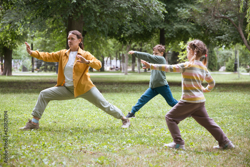 Family mom and two kids practice Tai Chi Chuan in a park. Chinese management skill Qi's energy.