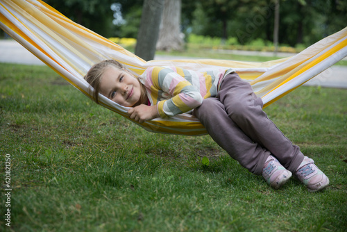 child girl lies in a hammock and have fun in the park in the summer