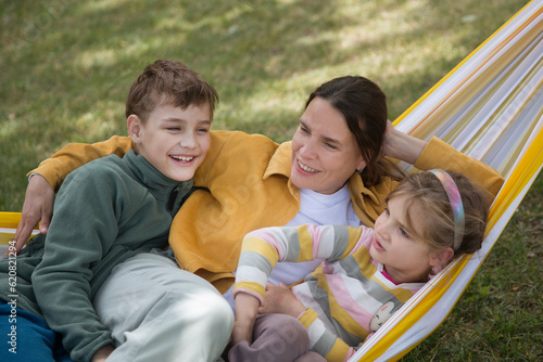 mom and Two kids swing in a hammock in a summer park or garden. Concept of friendly family.