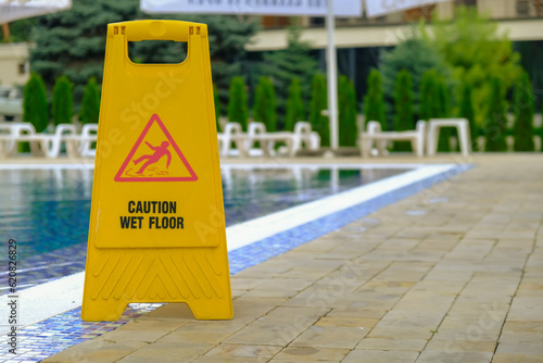 Caution wet floor warning sign near swimming pool in hotel.