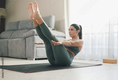 Focused sportswoman performing Navasana pose at home