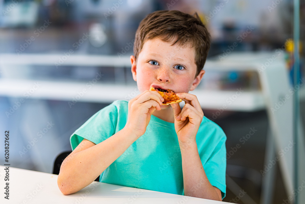 Little boy sitting at table in kitchen while eating pizza Little boy sitting at table in kitchen while eating pizza
