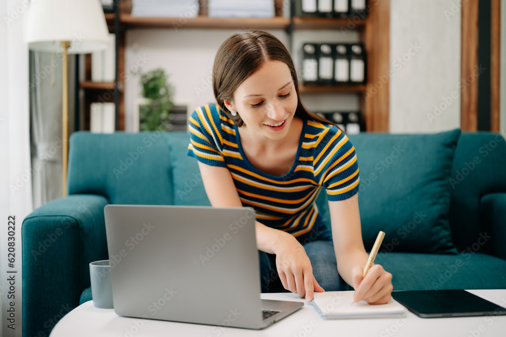 Confident Caucasian woman with a smile standing holding notepad and tablet in living room on the sofa at office Confident Caucasian woman with a smile standing holding notepad and tablet in living room on the sofa at office