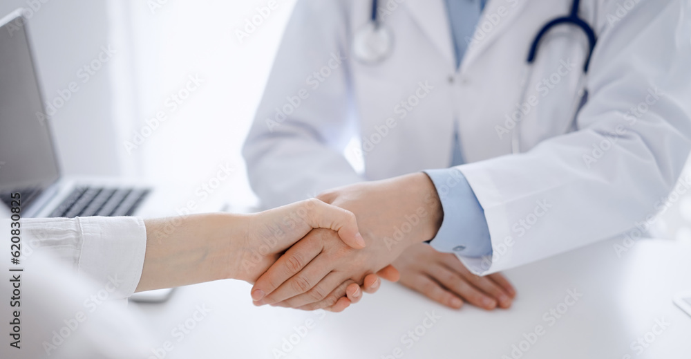 Doctor and patient shaking hands while sitting opposite of each other at the table in clinic, just hands close up. Medicine concept Doctor and patient shaking hands while sitting opposite of each other at the table in clinic, just hands close up. Medicine concept