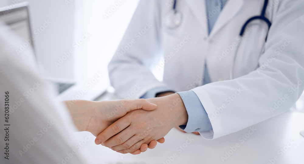 Obraz premium Doctor and patient shaking hands while sitting opposite of each other at the table in clinic, just hands close up. Medicine concept