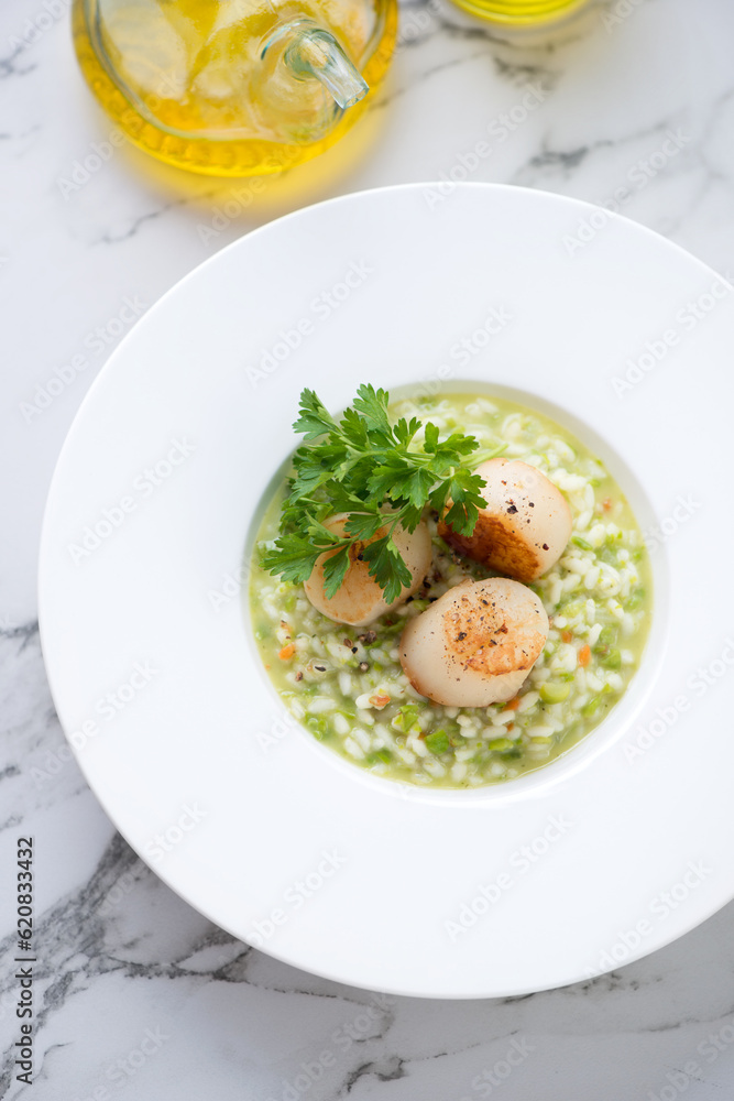Pea risotto with pan seared scallops served in a white plate, above view on a light-grey marble background, vertical shot Pea risotto with pan seared scallops served in a white plate, above view on a light-grey marble background, vertical shot