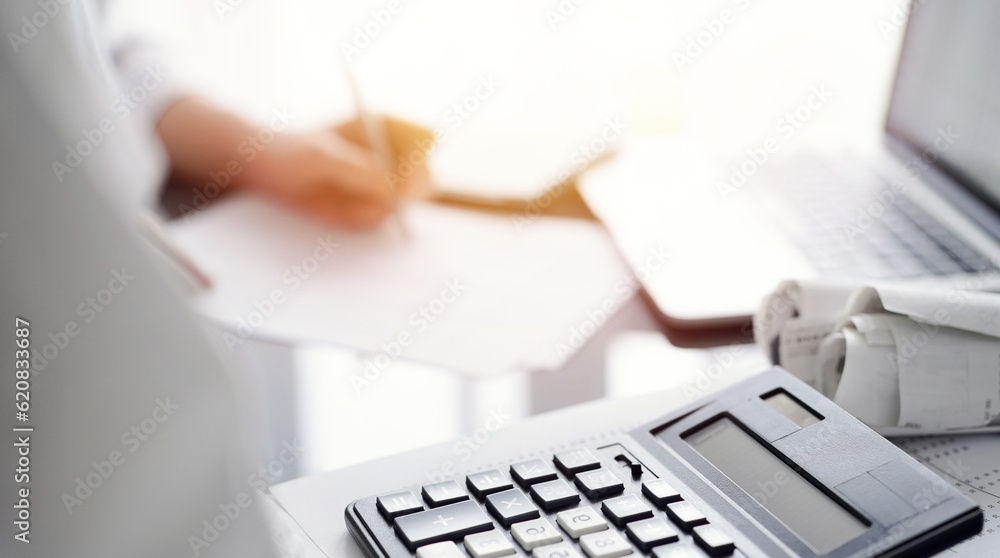 Woman accountant using a pen and laptop computer while counting and discussing taxes with a client, focus on the calculator. Business audit and finance concepts Woman accountant using a pen and laptop computer while counting and discussing taxes with a client, focus on the calculator. Business audit and finance concepts