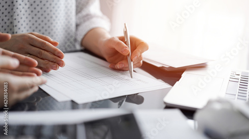 Woman accountant using a calculator and laptop computer while counting and discussing taxes with a client. Business audit and finance concepts